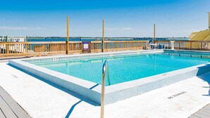 A rectangular swimming pool with a wooden deck surrounding it, a wooden fence, and a clear blue sky in the background. - Buena Vida Townhomes by Southern Vacation Rentals (Navarre)