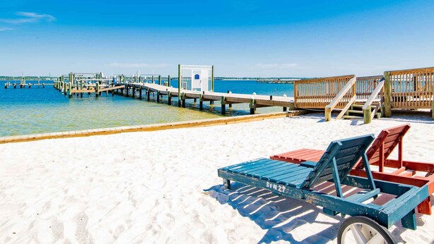 A beach with a wooden pier extending into the water, a lifeguard stand, and a beach chair. - Buena Vida Townhomes by Southern Vacation Rentals (Navarre)