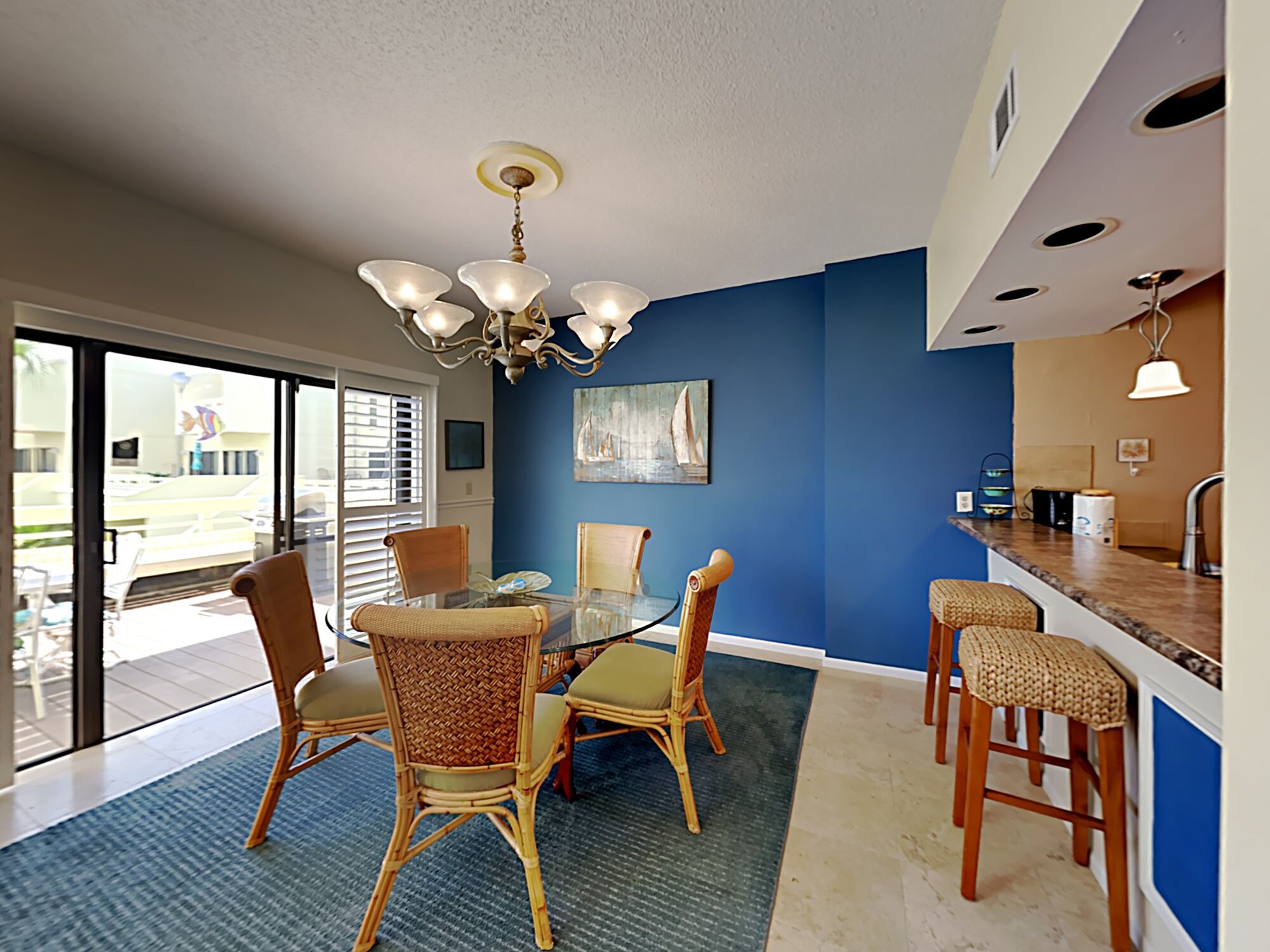 A dining area with wicker chairs, a glass table, and a chandelier.