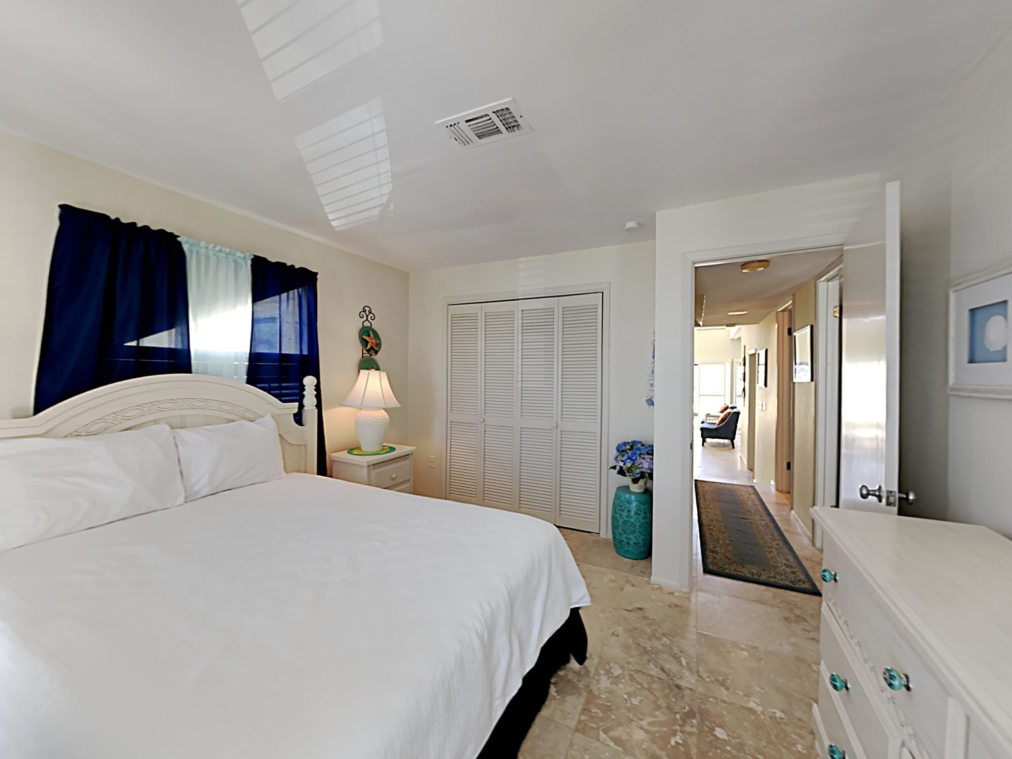 A bedroom with a large bed, a bedside table with a lamp, a closet, and a dresser.