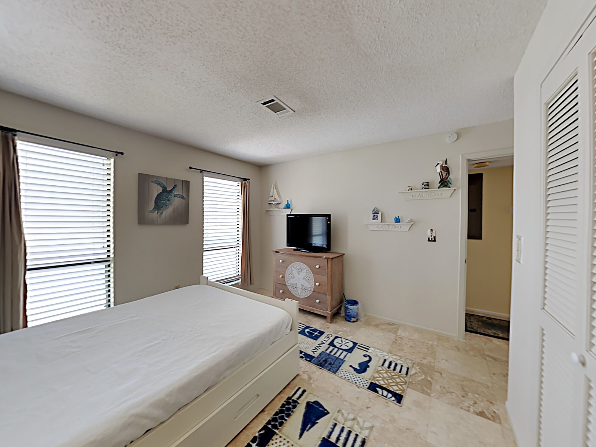A bedroom with a bed, a television on a wooden dresser, a small sailboat decoration, and a patterned rug.