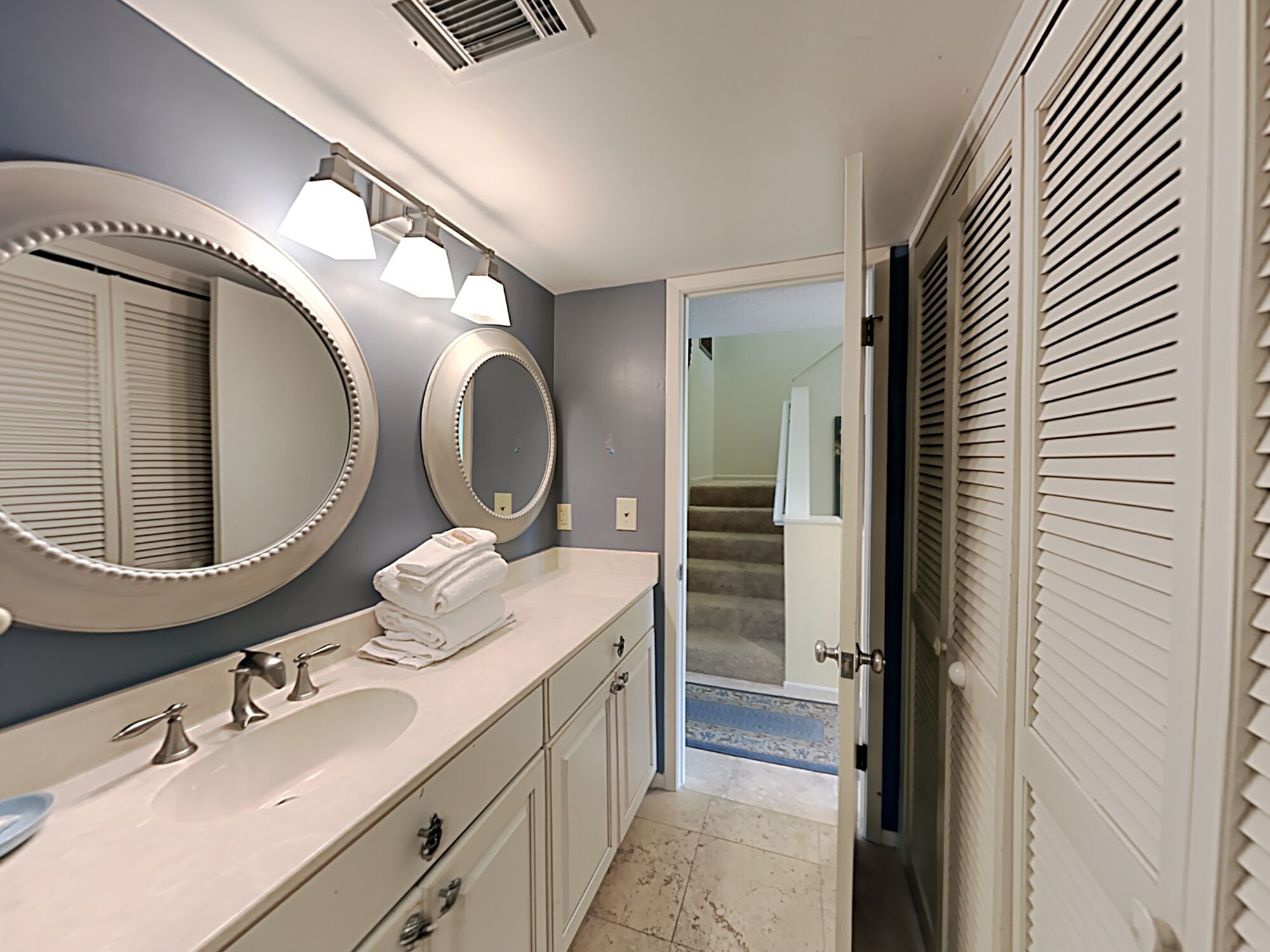 A bathroom with a large mirror, two sinks, and a towel stack.
