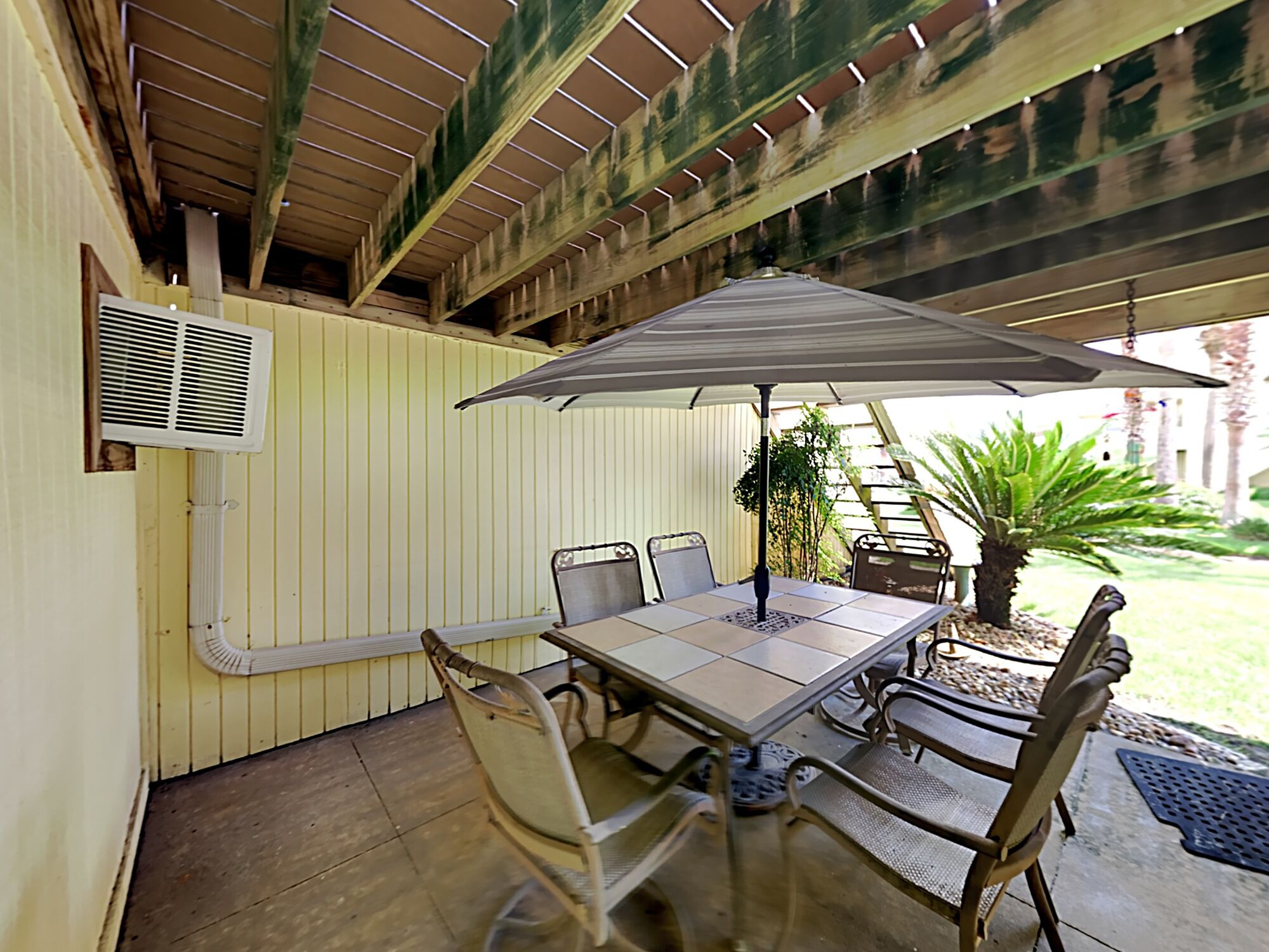 Une terrasse extérieure avec une table et des chaises, un parasol et un escalier menant à un niveau supérieur.