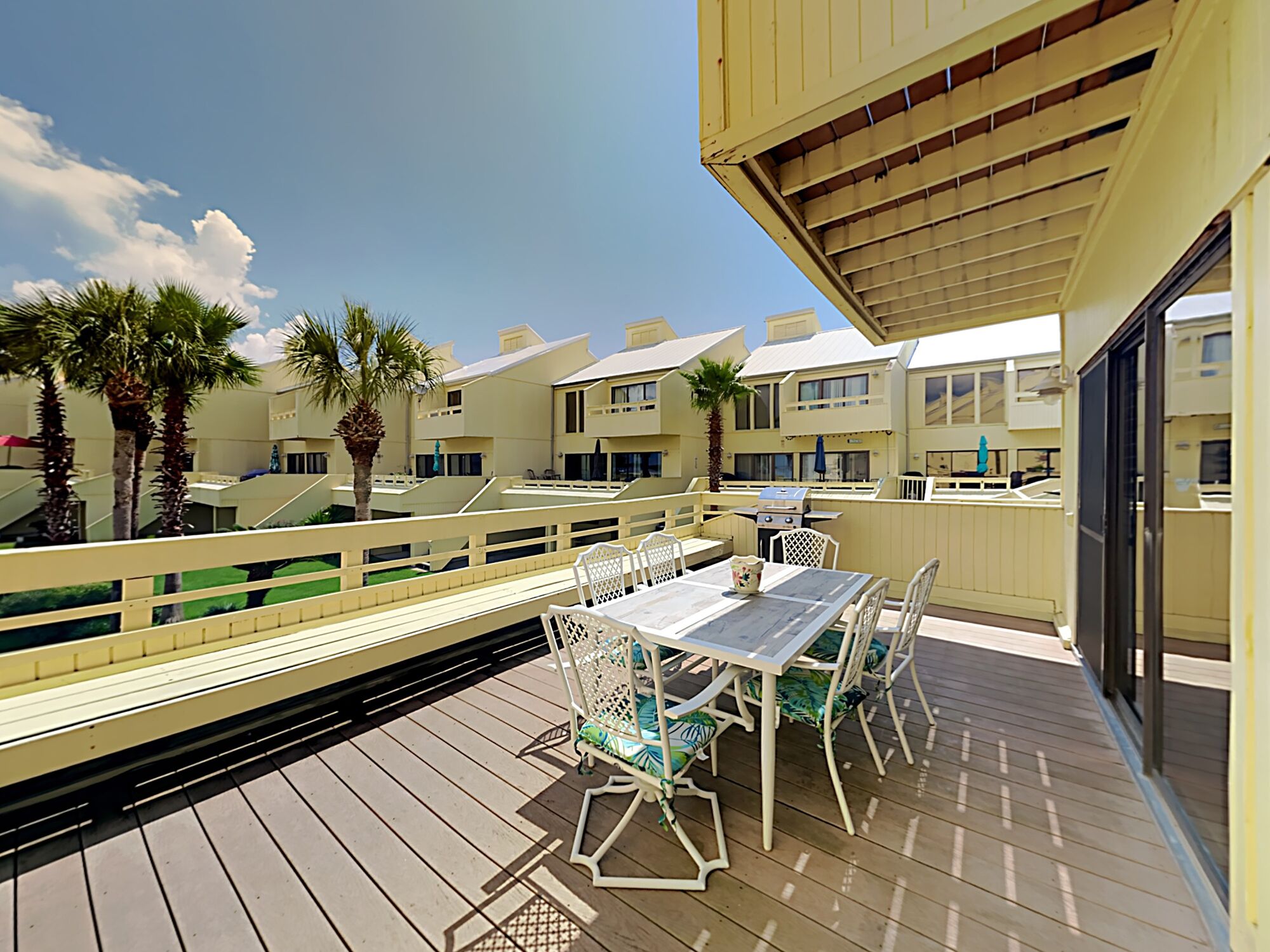 A deck with outdoor furniture, a grill, and palm trees.