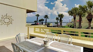 A deck with a table and chairs, overlooking a beach with palm trees and a clear sky. - Buena Vida Townhomes by Southern Vacation Rentals (Navarre)