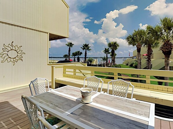 Una terraza con mesa y sillas, con vistas a una playa con palmeras y un cielo despejado.