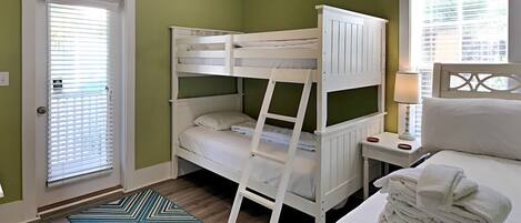 A bunk bed room with a door, a bedside table with a lamp, and a patterned rug.