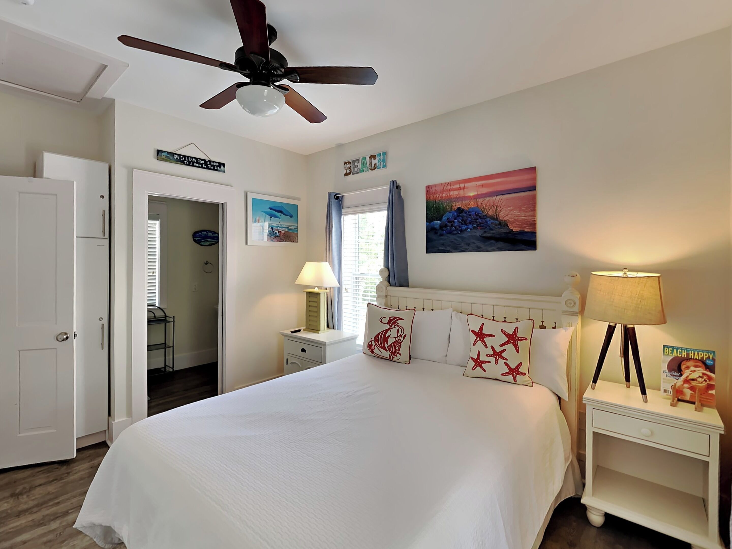 A bedroom with a bed, a ceiling fan, a nightstand, a lamp, a painting, and a door.