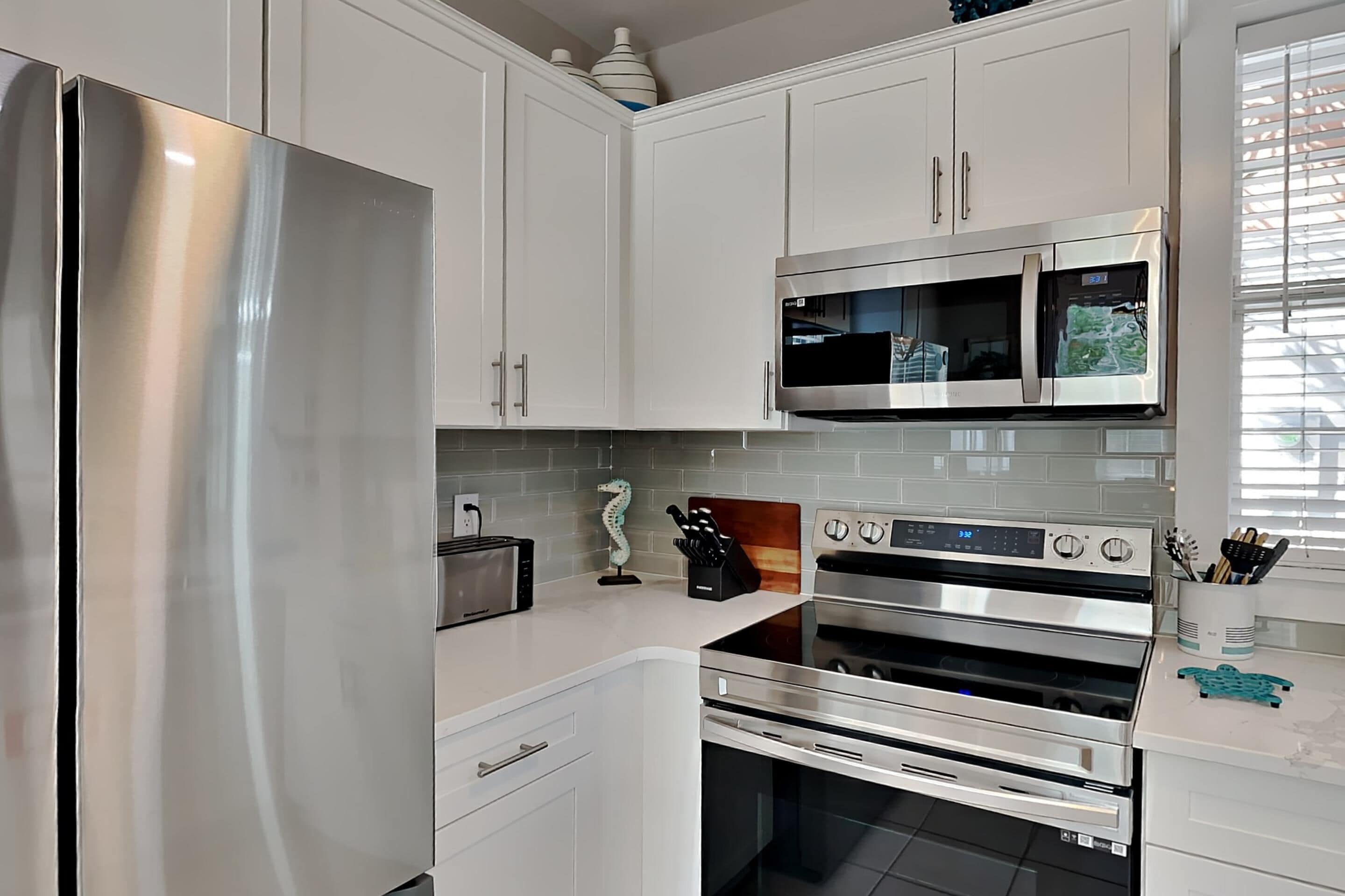 A modern kitchen with stainless steel appliances, white cabinetry, and a tiled backsplash.