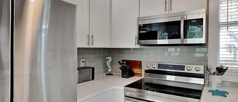 A modern kitchen with stainless steel appliances, white cabinetry, and a tiled backsplash.