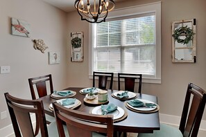 A dining room with a round table set for six, surrounded by wooden chairs.
