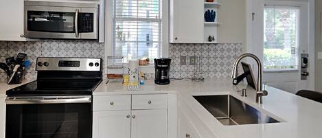 A modern kitchen with white cabinetry, stainless steel appliances, and a large island with a sink.