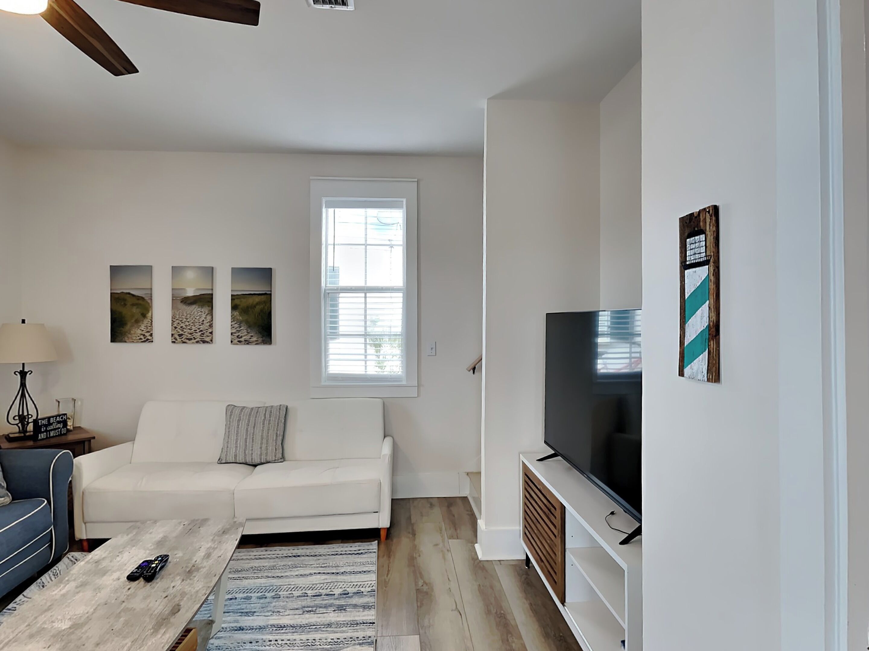 A living room with a white sofa, a coffee table, a TV, and three framed pictures on the wall.
