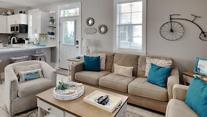 A modern living room with a beige sofa, a coffee table, and a dining area with a kitchen in the background. - Bungalows at Seagrove by Southern Vacation Rentals (Santa Rosa Beach)