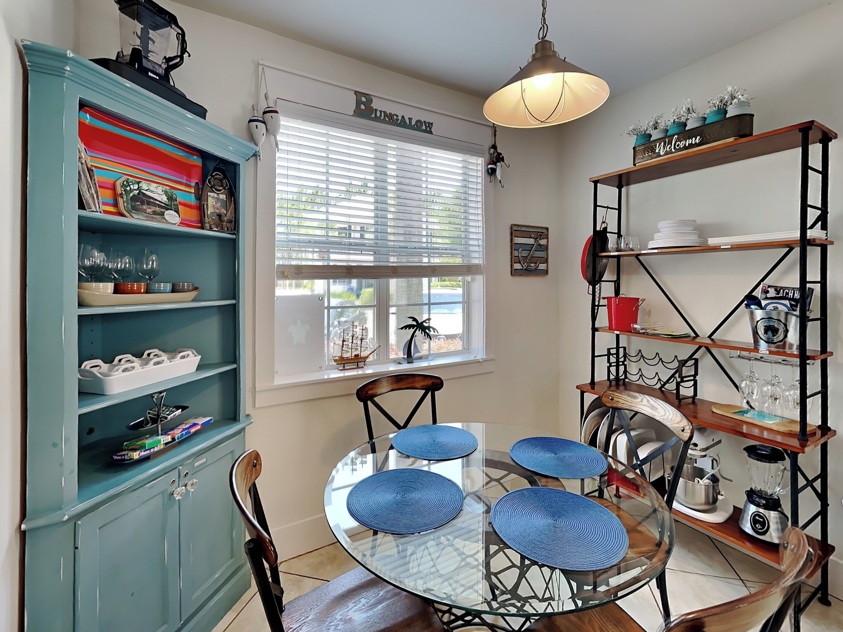 A kitchen with a round glass table, blue chairs, and a teal cabinet.