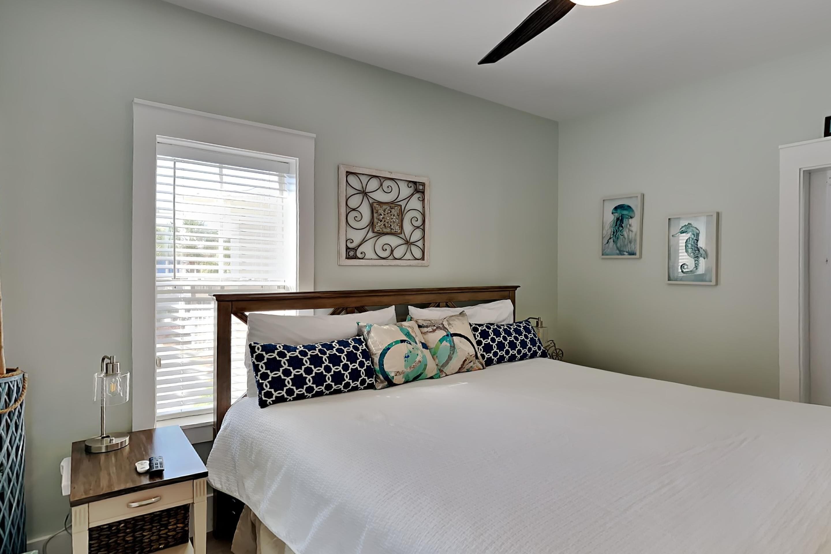A bedroom with a bed, bedside table, lamp, and artwork on the wall.