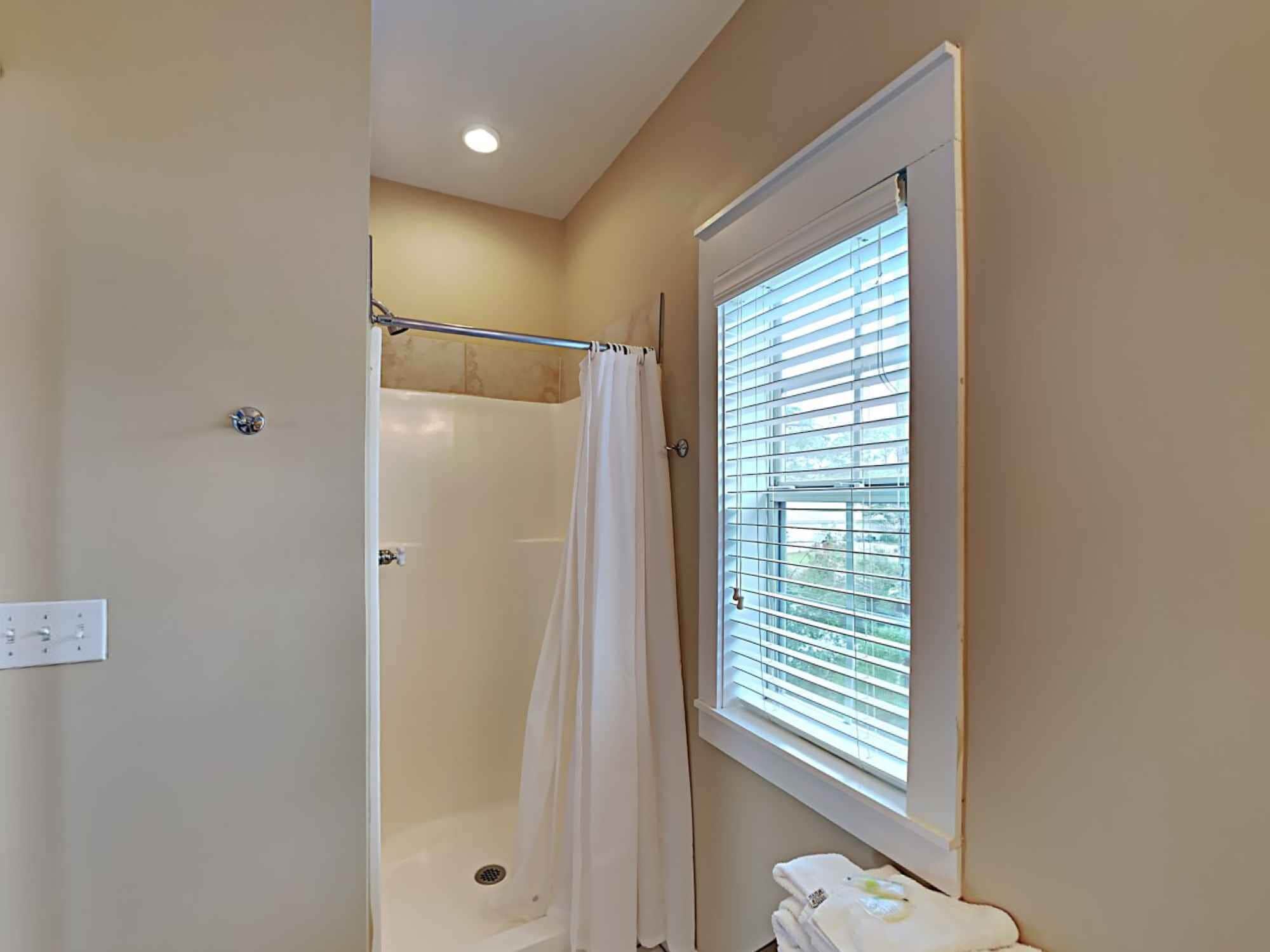Une salle de bain avec une douche, une fenêtre avec des stores et un porte-serviettes.
