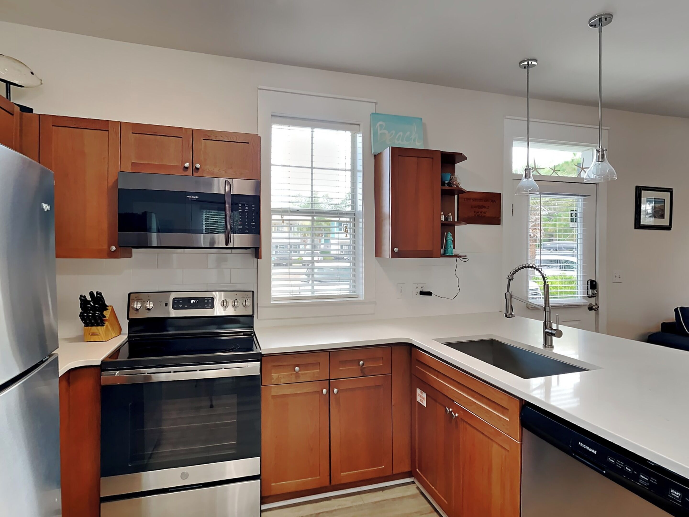 A modern kitchen with stainless steel appliances, wooden cabinets, a built-in oven, and a large window.