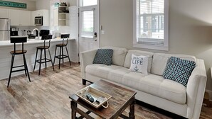 A modern living room with a white sofa, two bar stools, a coffee table, and a kitchen in the background. - Bungalows at Seagrove by Southern Vacation Rentals (Santa Rosa Beach)