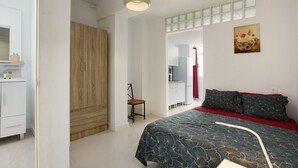 A bedroom with a bed, a wooden wardrobe, a chair, a mirror, and a painting on the wall.