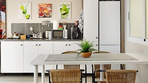 A modern kitchen with white cabinets, a dining table with wicker chairs, and a potted plant.