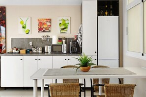 Uma cozinha moderna com armários brancos, uma mesa de jantar com cadeiras de vime e uma planta em vaso.