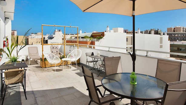A rooftop terrace with outdoor seating, including a round table and chairs, a large umbrella, and a view of the cityscape.