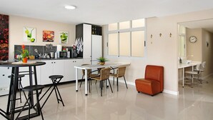 A modern kitchen with white cabinets, a dining table with four chairs, a small orange chair, and a refrigerator.