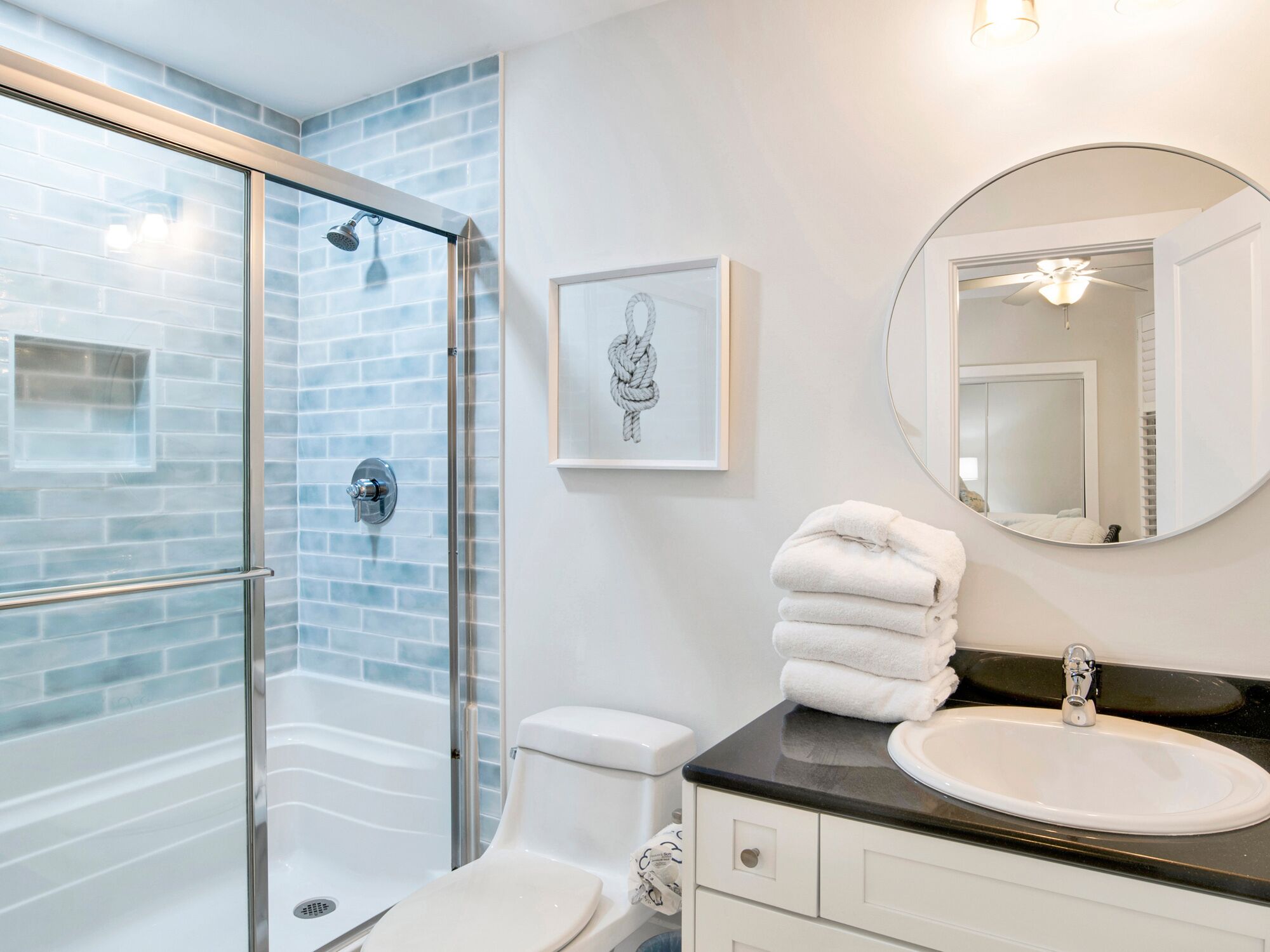 A bathroom with a glass shower enclosure, a toilet, a sink, and a mirror.