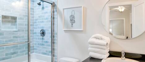 A bathroom with a glass shower enclosure, a toilet, a sink, and a mirror.