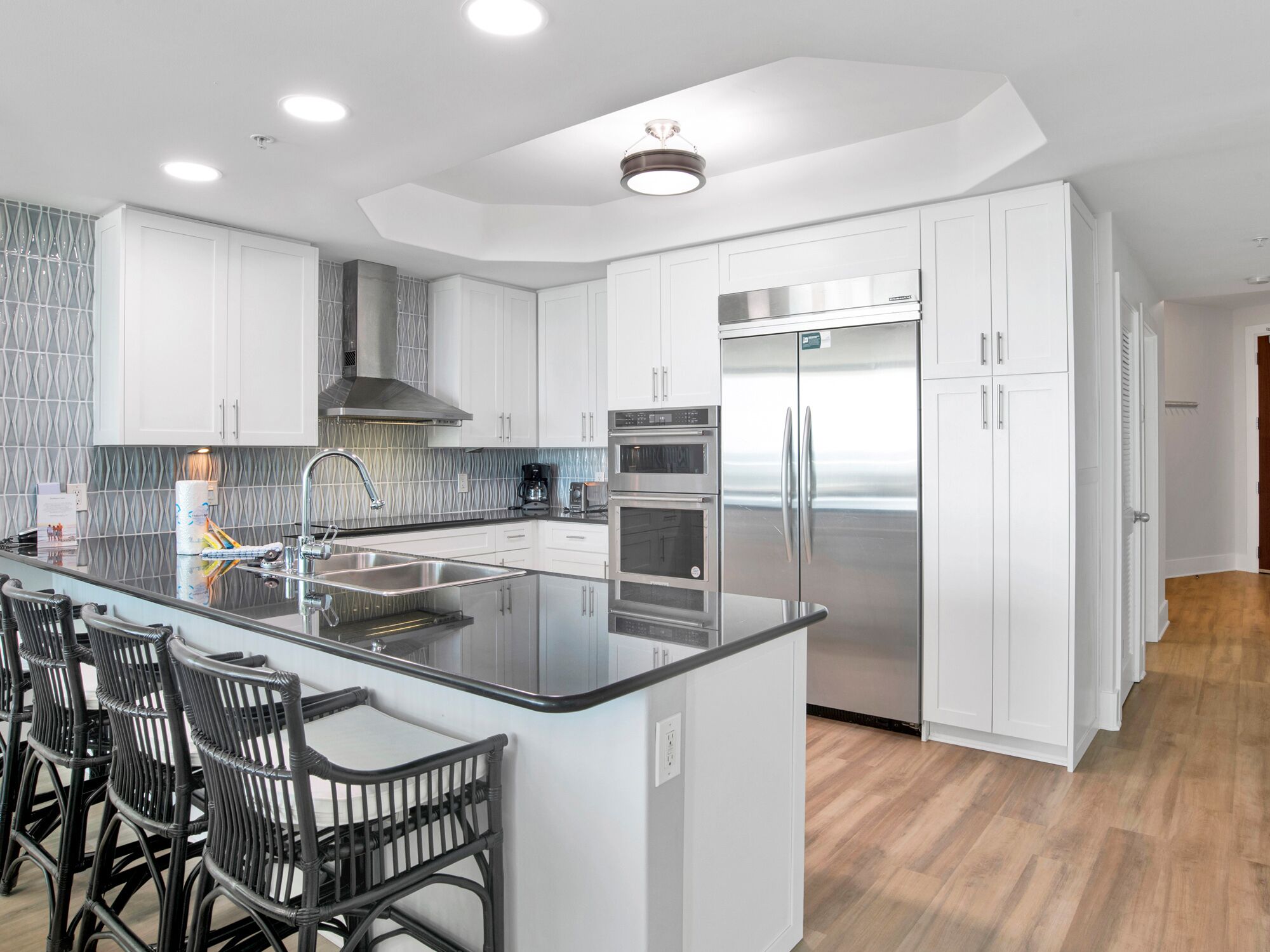 Una cocina moderna con armarios blancos, un refrigerador de acero inoxidable y una isla de encimera negra con taburetes de bar.