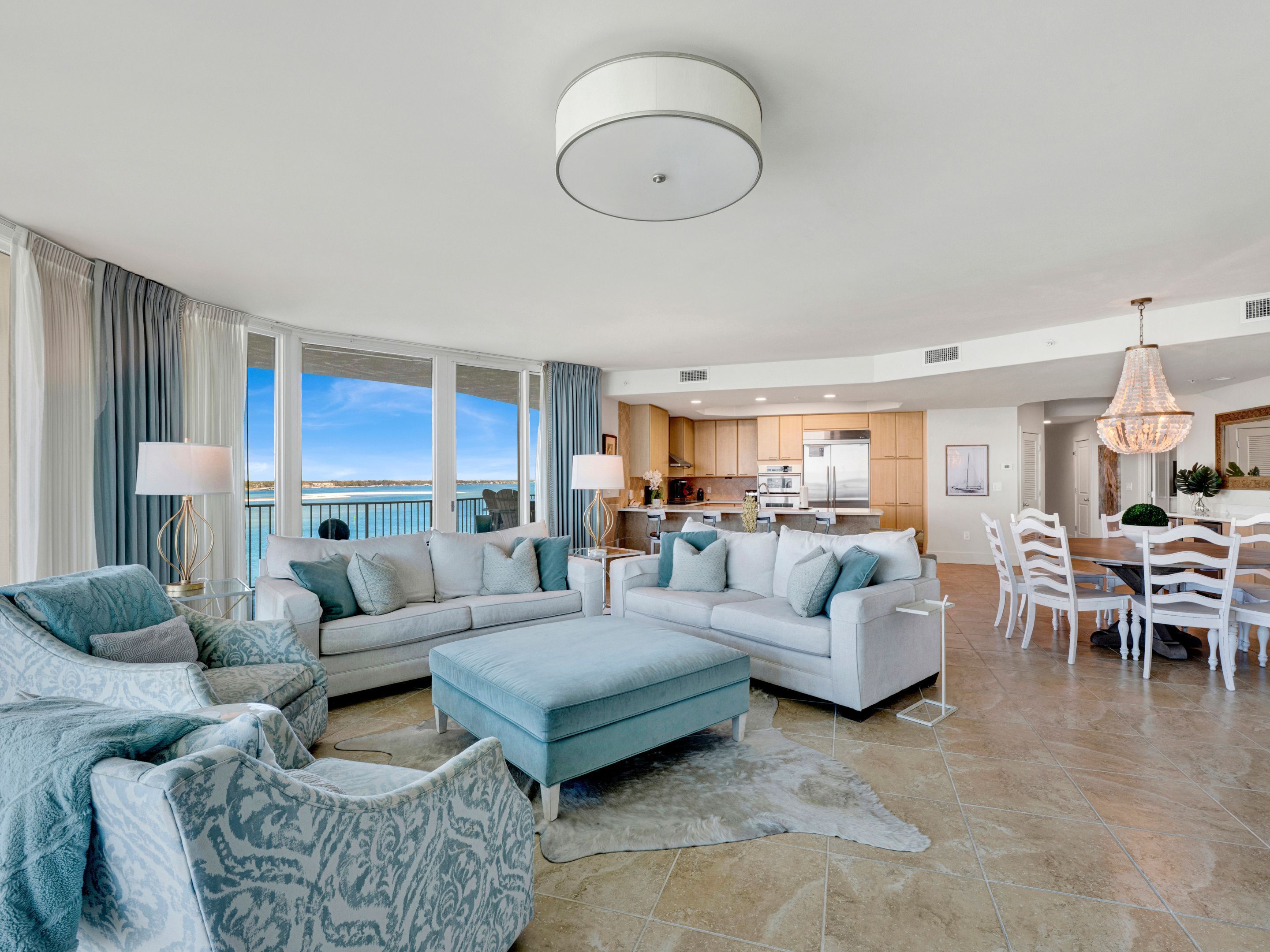 A spacious living room with a large sectional sofa, a dining area with white chairs, and a kitchen in the background.