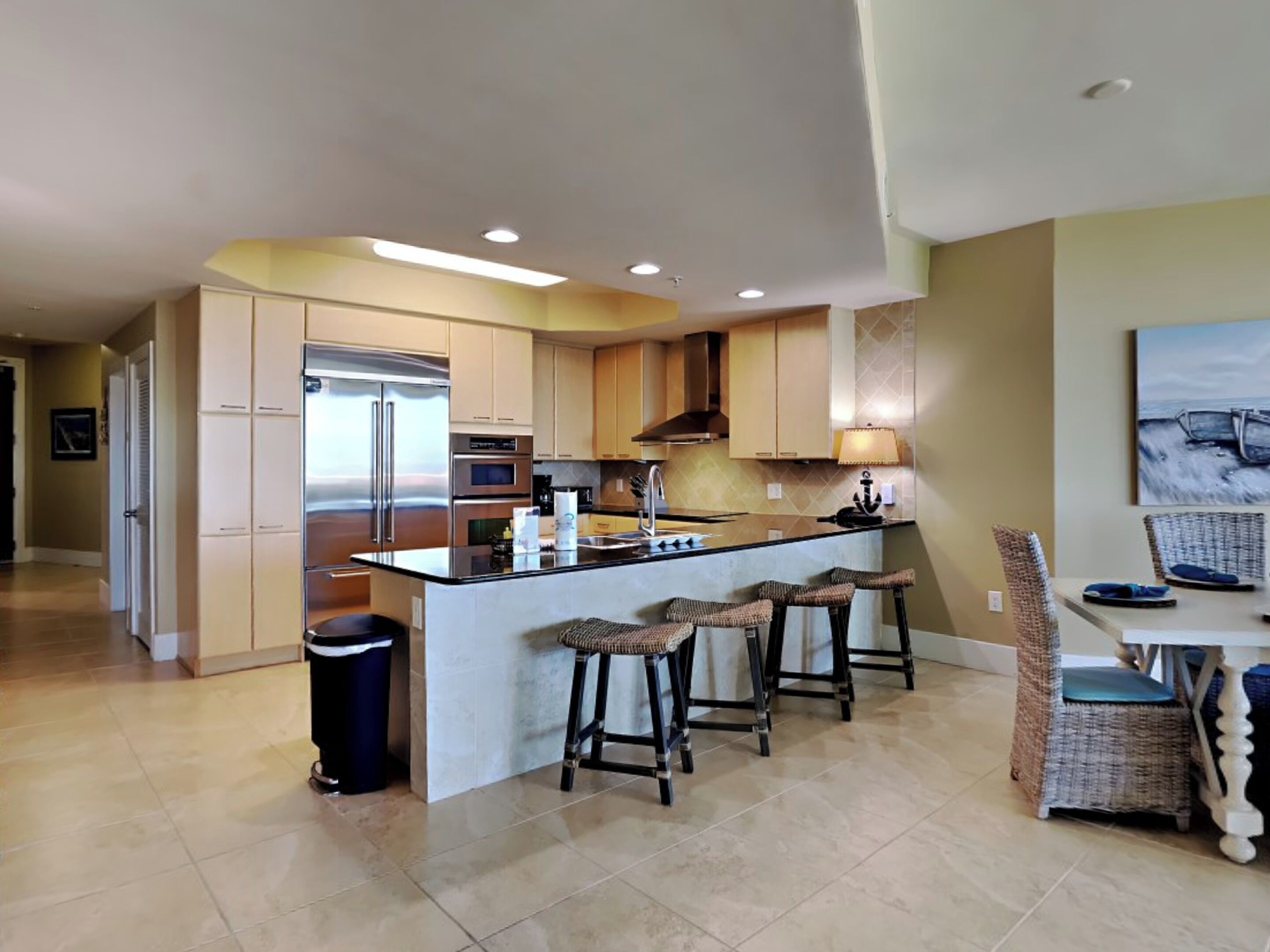 A modern kitchen with a central island, bar stools, and a trash can.