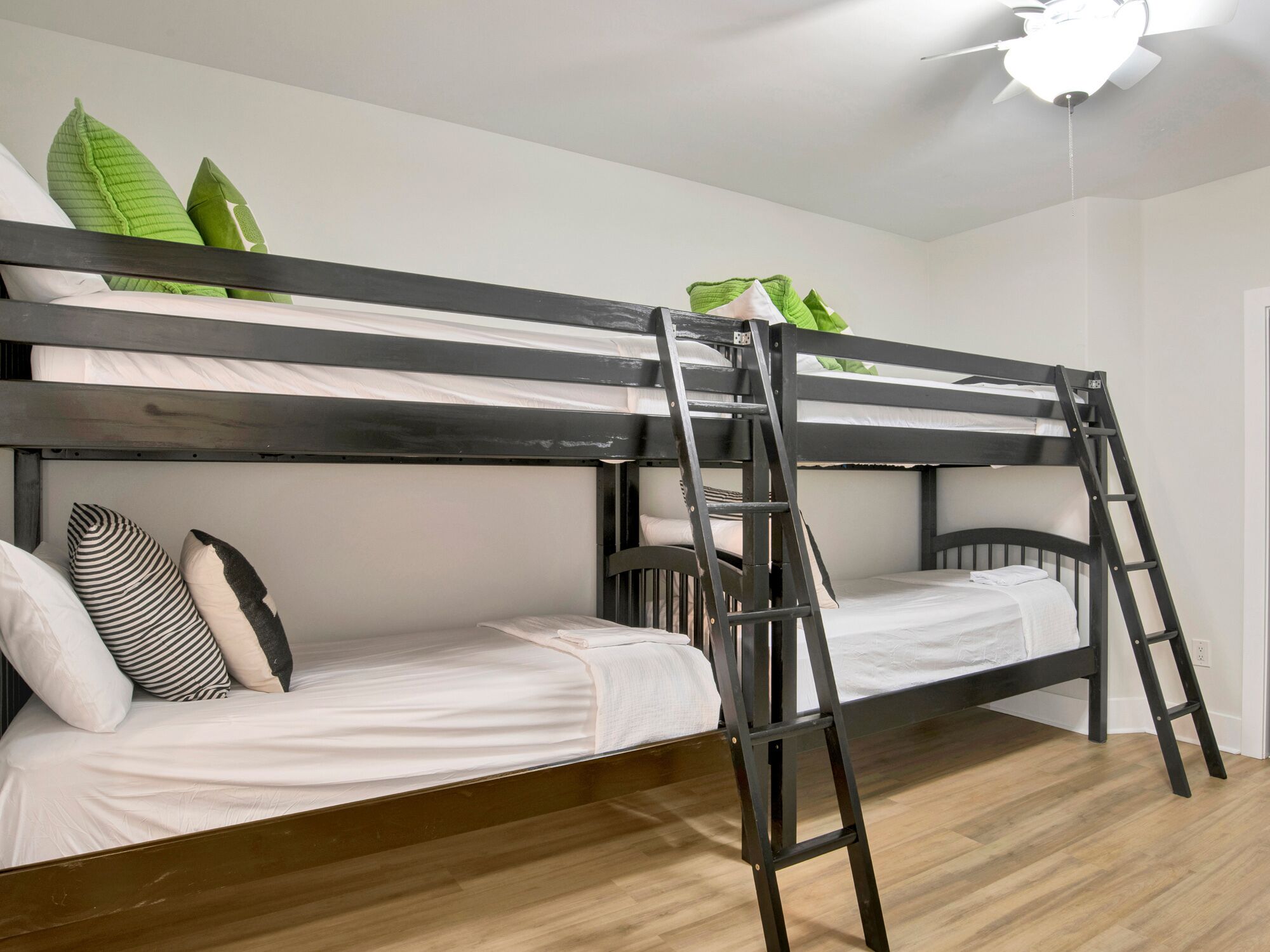 Ein Stockbett mit einer Leiter, weißer Bettwäsche und grünen Kissen.