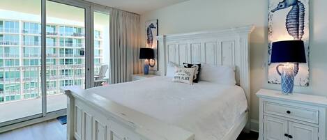 A spacious bedroom with a large bed, a ceiling fan, and a view of a building through a sliding glass door.