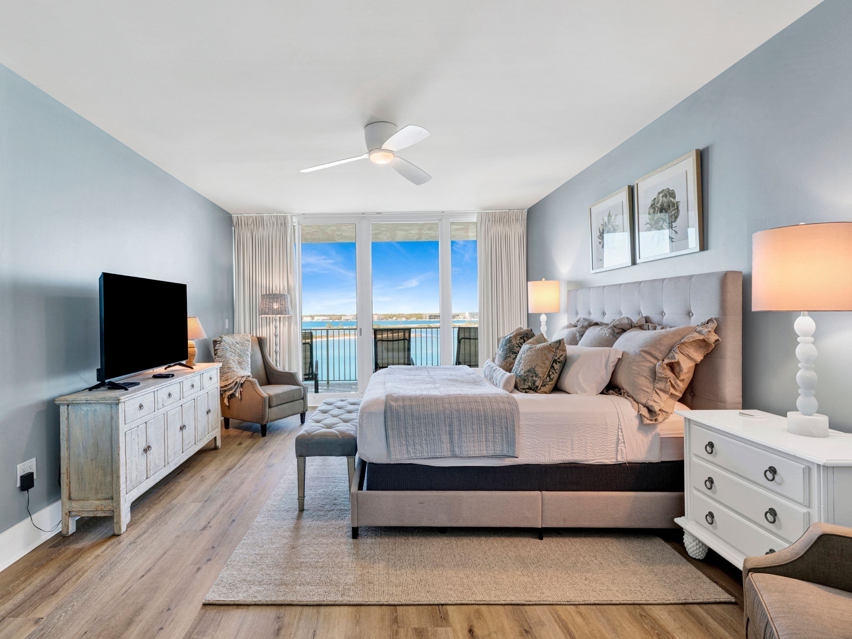 Ein modernes Schlafzimmer mit einem großen Bett, einem Fernseher, einem Deckenventilator und Meerblick.