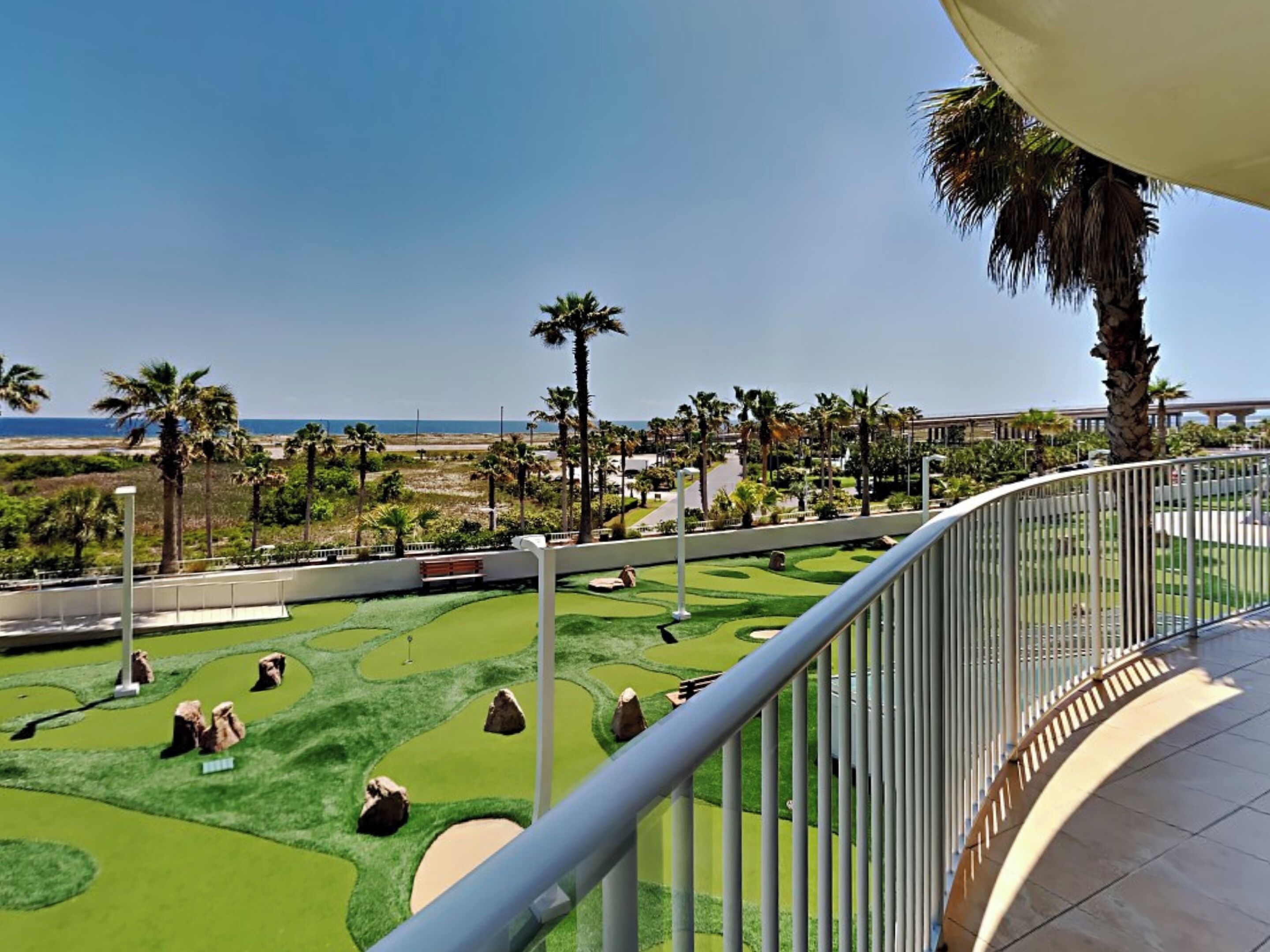A golf course with a clear view of the ocean and palm trees.