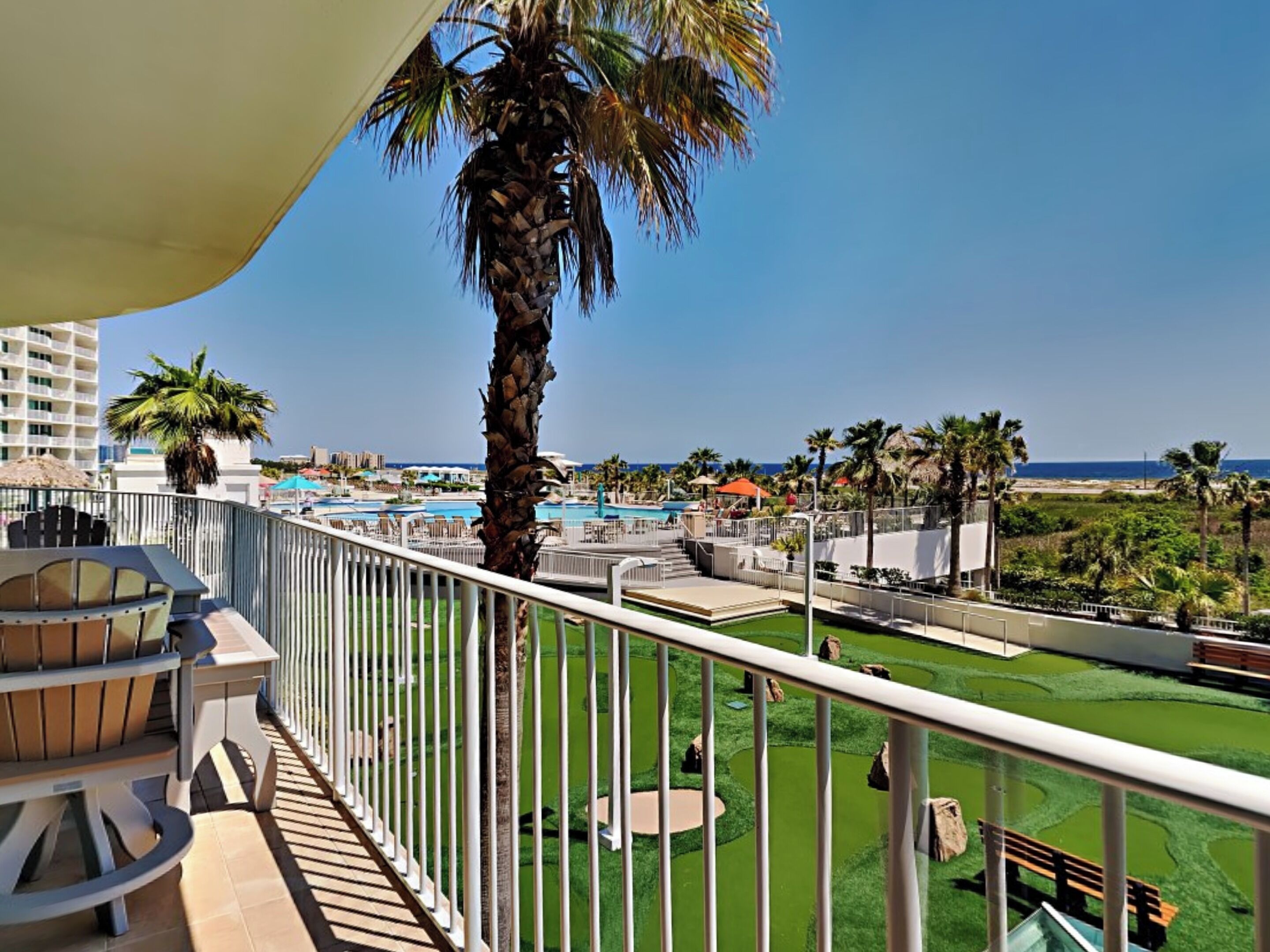 Een balkon met uitzicht op een zwembad, palmbomen en een golfbaan.