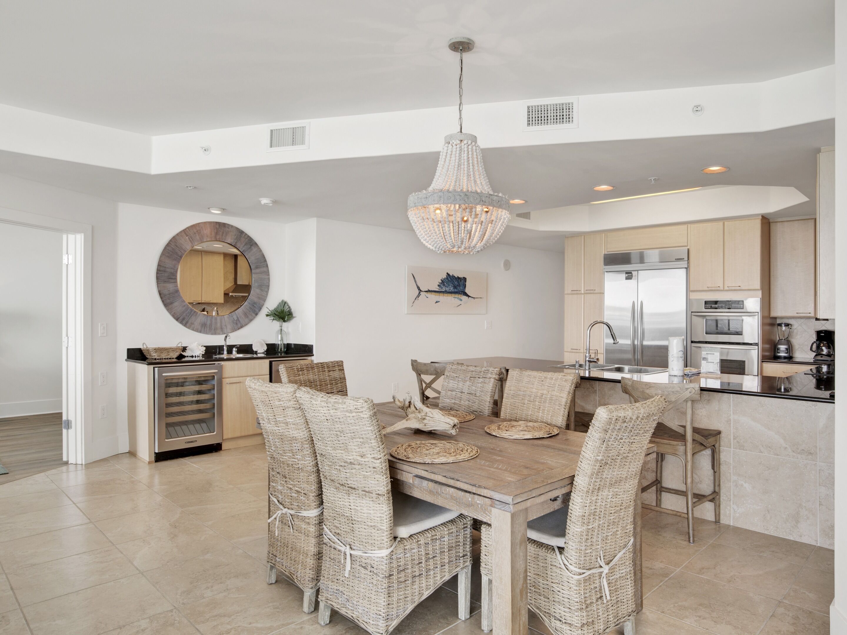 A modern kitchen with stainless steel appliances, a dining area with wicker chairs, and a chandelier.