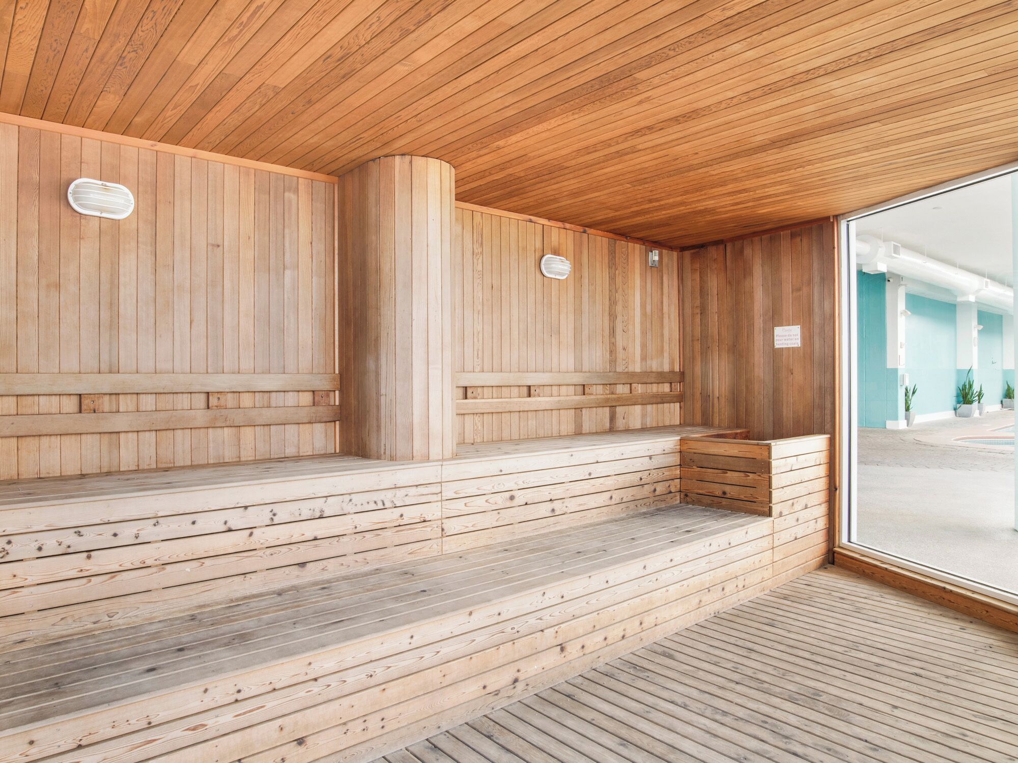 A sauna with wooden benches and a wooden floor, large windows, and a wooden ceiling.