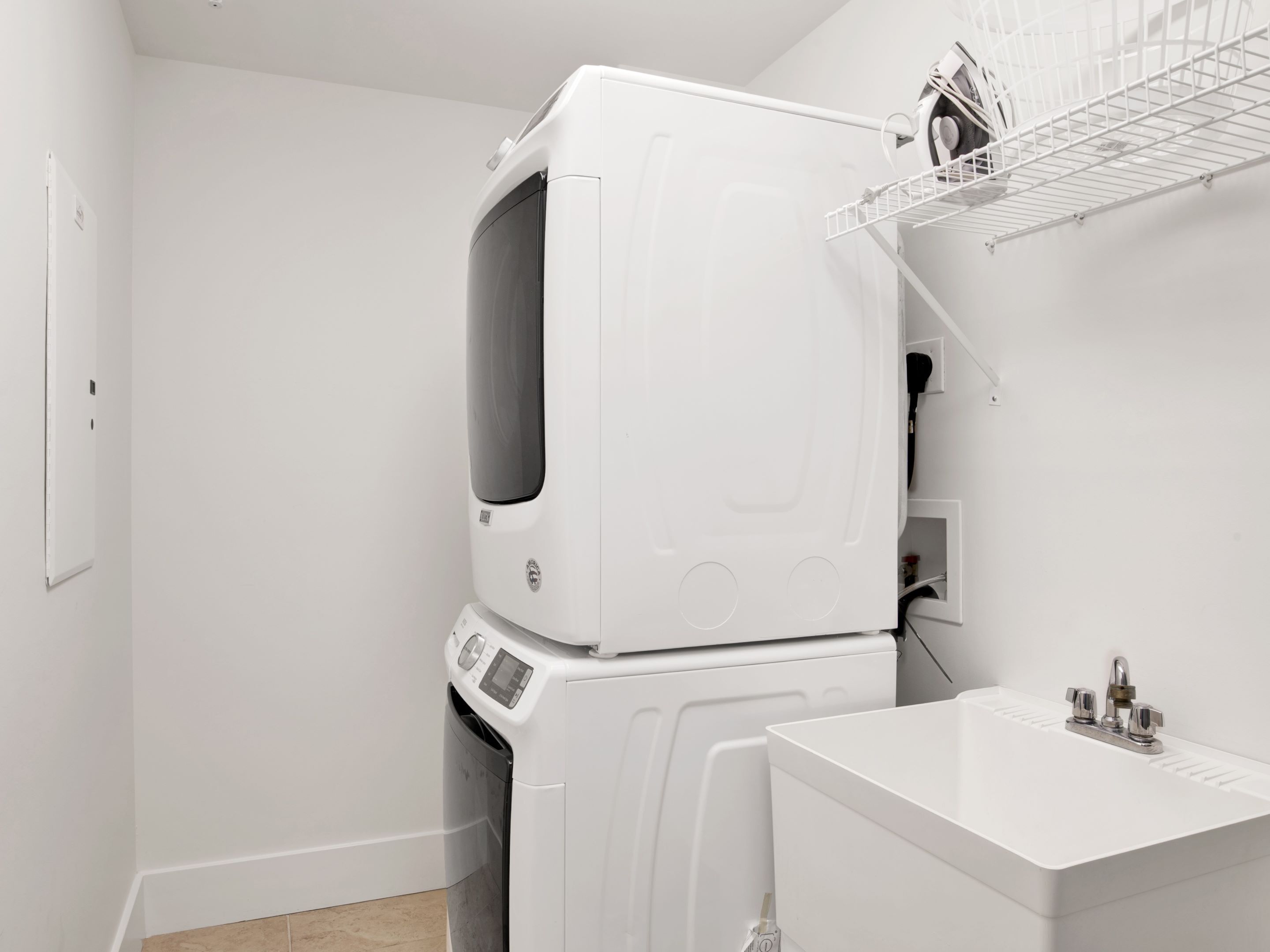 A laundry room with stacked washer and dryer, a white sink, and a metal drying rack.