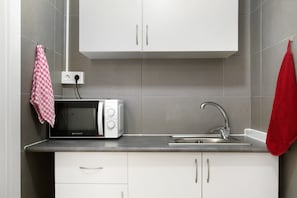 Una cocina con microondas, pileta, alacenas y un enchufe.