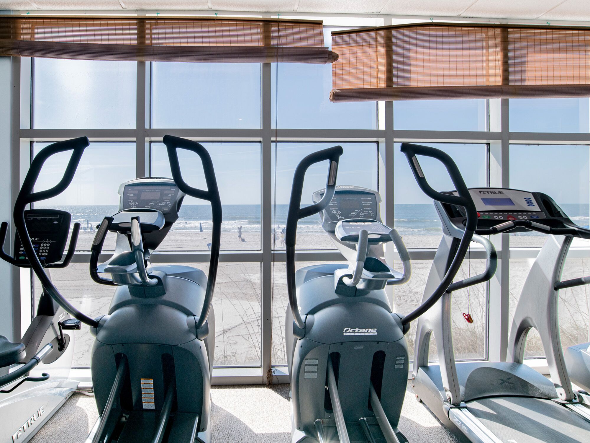 Une salle de remise en forme équipée de vélos d’exercice et de tapis de course, avec de grandes fenêtres donnant sur la plage.