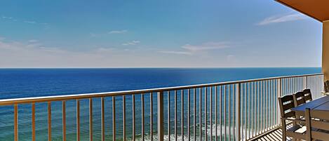 A balcony with a view of the ocean, a railing, and a table with chairs.