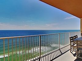 A balcony with a view of the ocean, a railing, and a table with chairs.