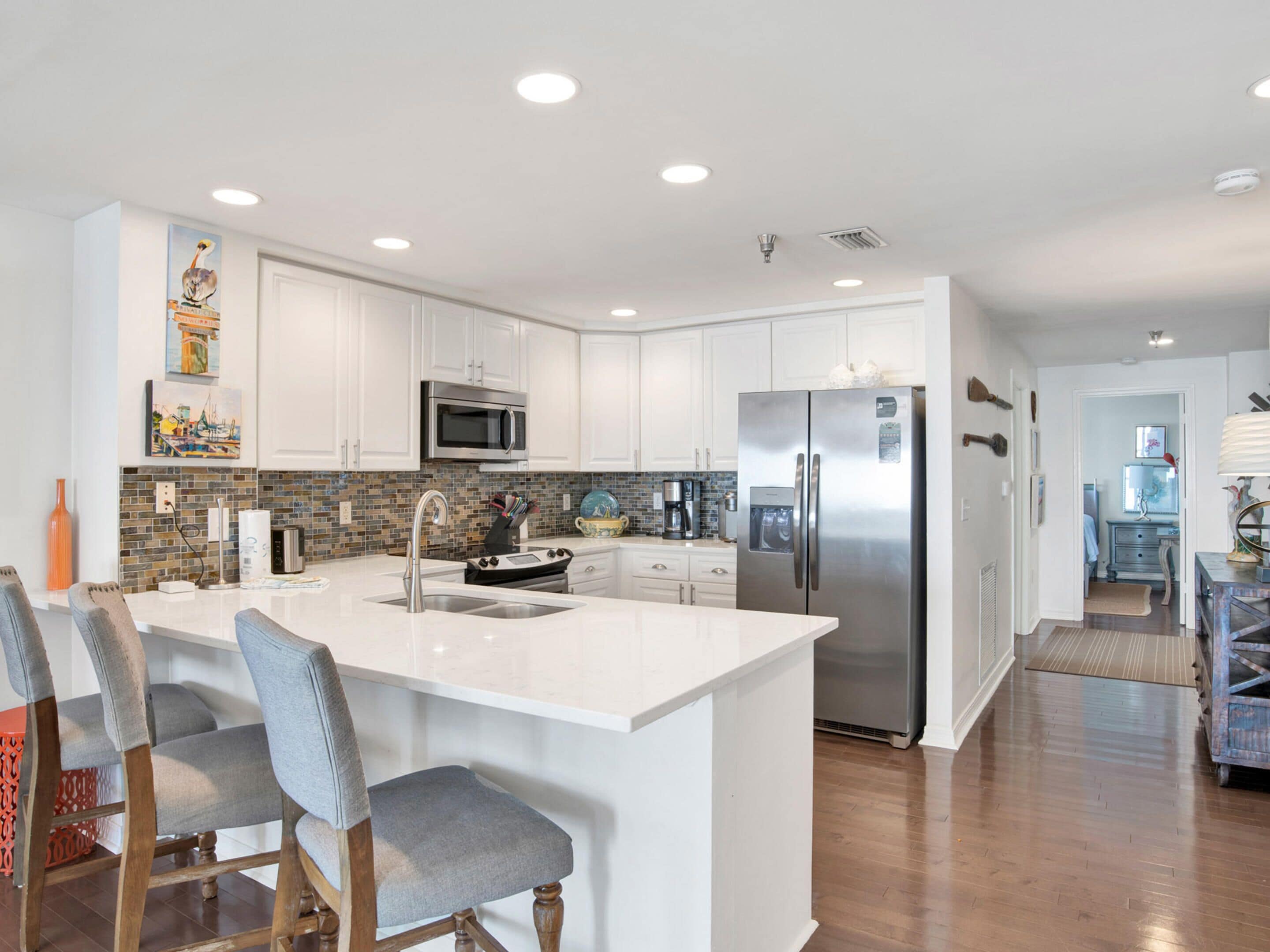 A modern kitchen with white cabinetry, stainless steel appliances, and a central island with bar stools.