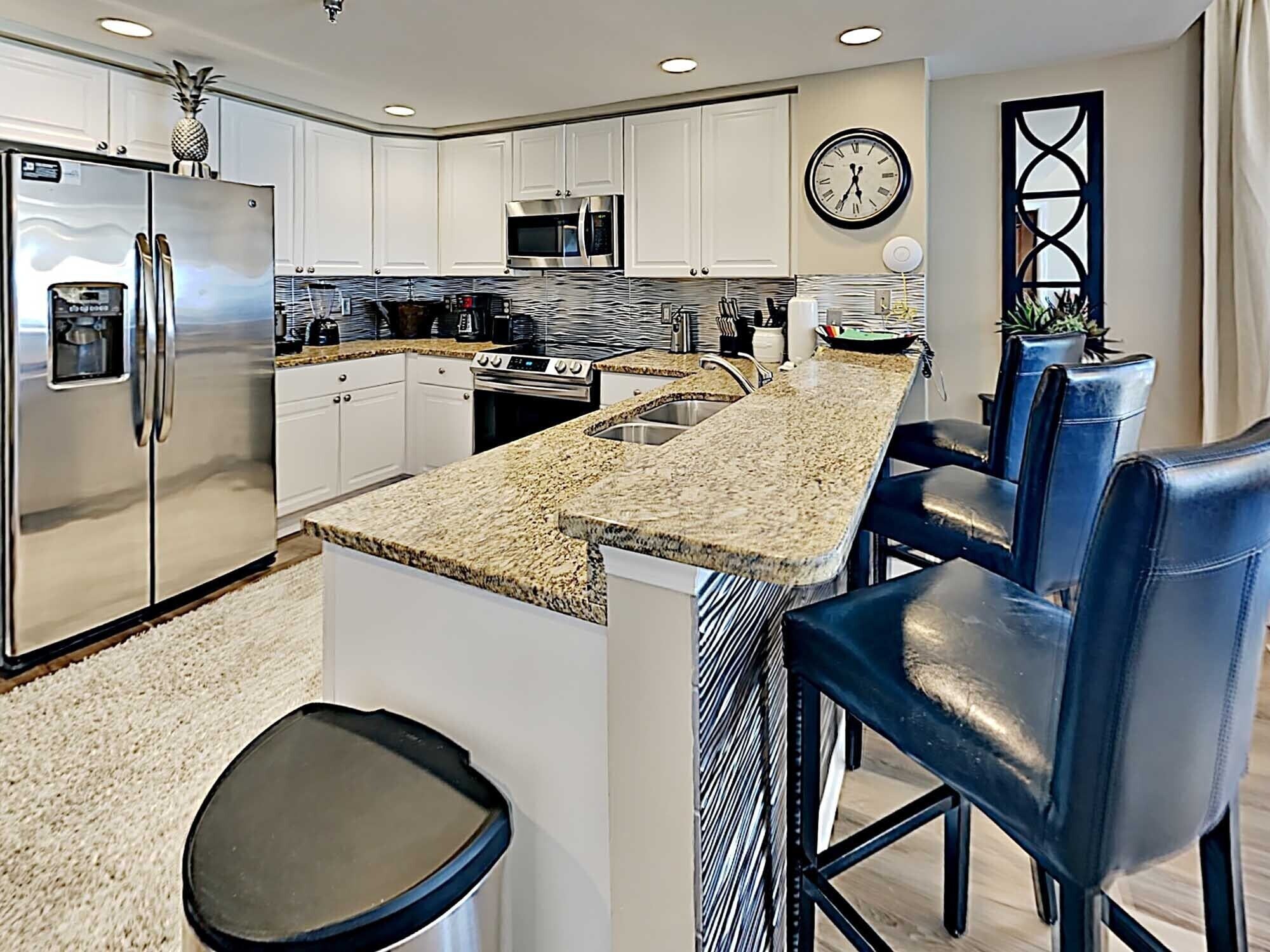 A modern kitchen with white cabinets, stainless steel appliances, a granite countertop, and a clock on the wall.