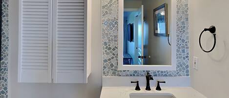 A bathroom with a white toilet, a white sink with a marble countertop, a mirror with a mosaic backsplash, and a towel ring on the wall.