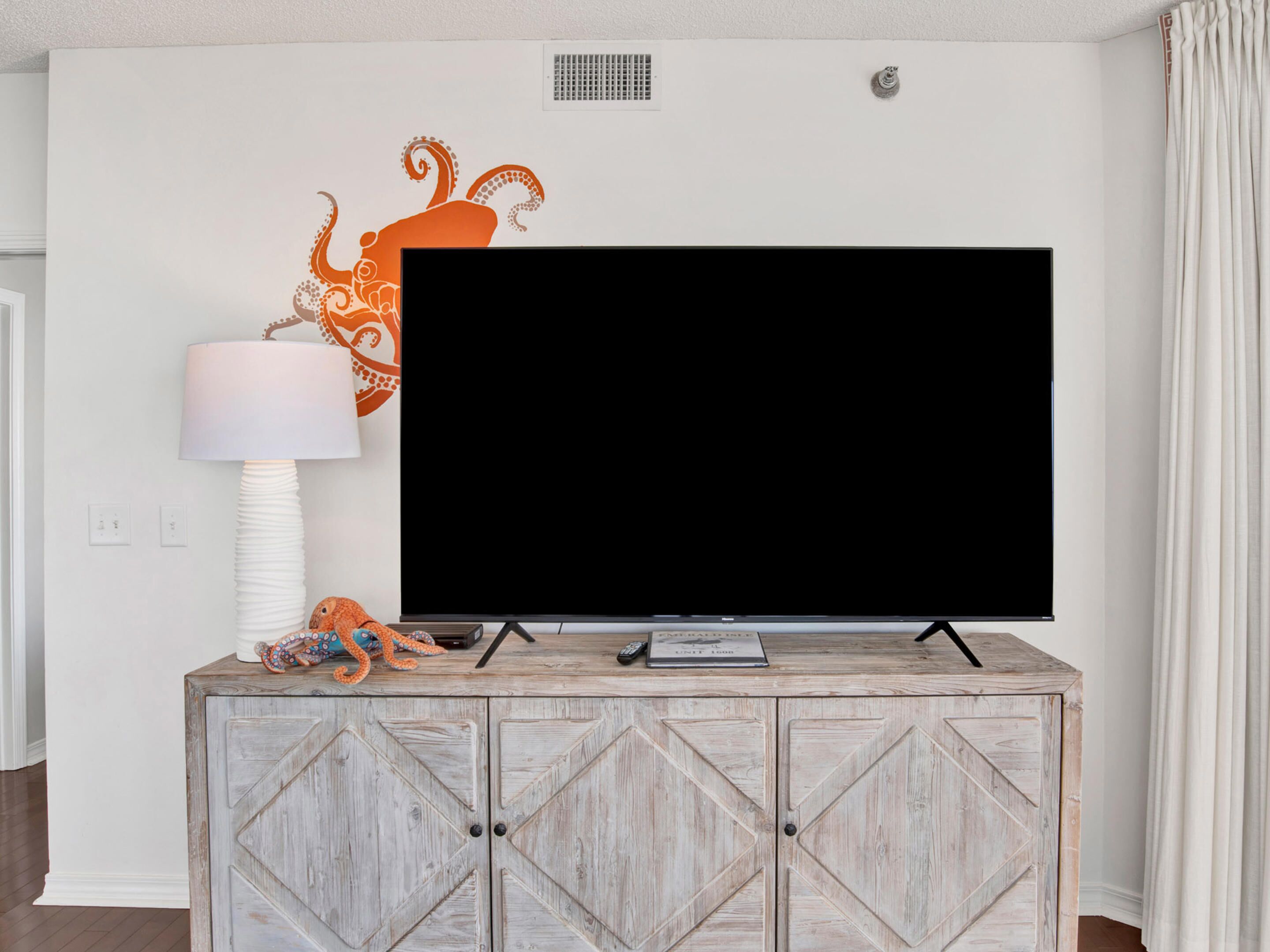 A flat-screen TV on a wooden cabinet with a decorative octopus mural on the wall behind it.