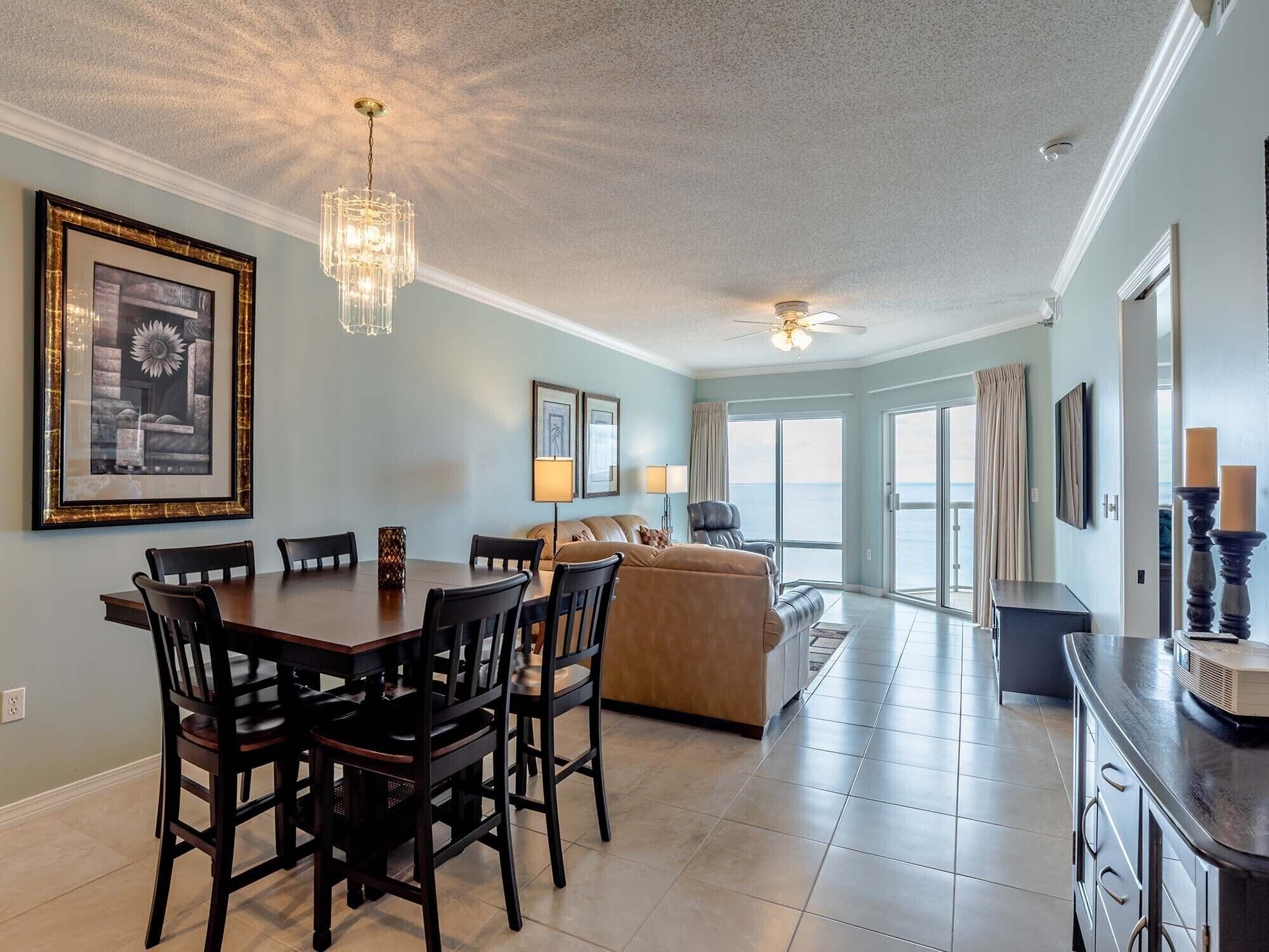A spacious living room with a dining area, a ceiling fan, and large windows offering a view of the outdoors.